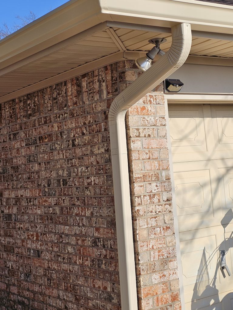 White gutter and downspout on the corner of a brick home, installed by Ace Renovations